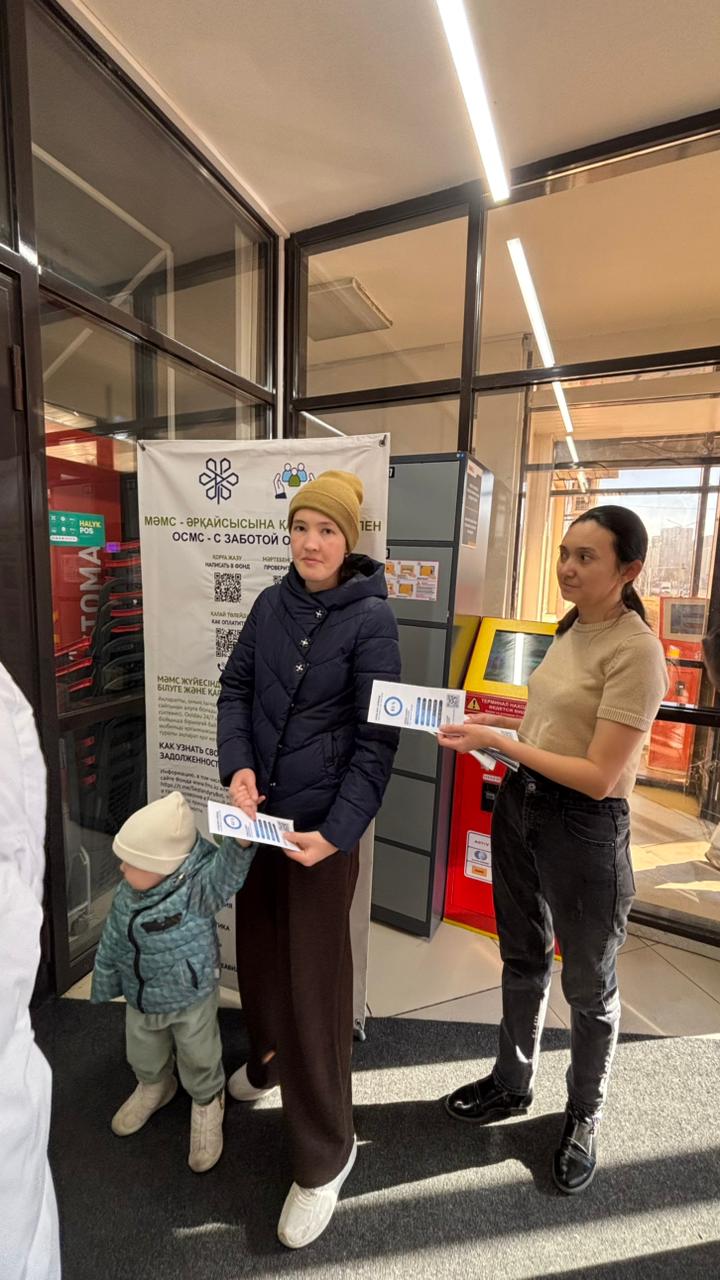 Сотрудница поликлиники раздаёт информационные буклеты по ОСМС посетителям с ребёнком
