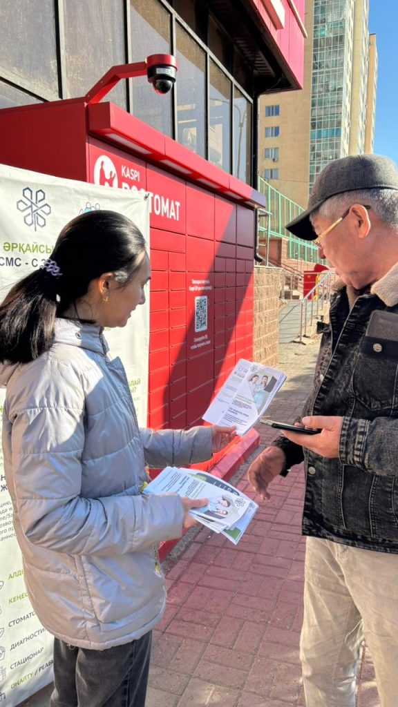 Медицинская работница раздаёт буклеты по ОСМС мужчине на улице возле поликлиники