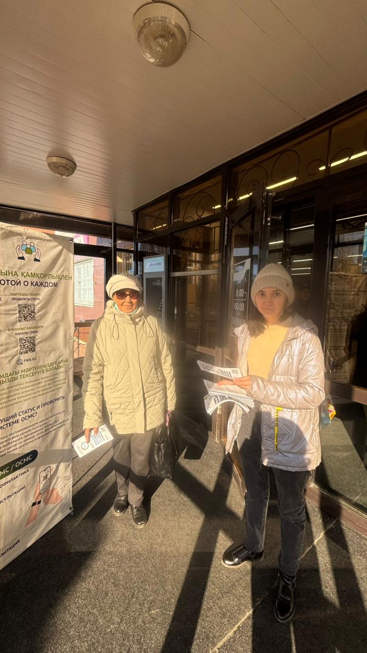 Сотрудница поликлиники проводит разъяснительную работу по ОСМС с пожилой женщиной у входа в здание